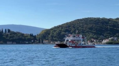 Huzurlu bir göl üzerinde yüzen bir su aracı görkemli dağlar ve yemyeşil ağaçlarla çevrili, çarpıcı bir doğal manzara yaratıyor.