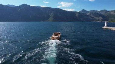 Huzurlu bir göl üzerinde yüzen bir tekne. Etrafı görkemli dağlarla çevrili, berrak gökyüzü altında ve kabarık bulutların altında. Doğal manzaranın ve su kaynaklarının güzelliğini gözler önüne seriyor.