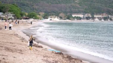 Bir kadın sahildeki doğal manzaranın tadını çıkarıyor, rüzgar dalgalarını hissederken sörf tahtasını tutuyor ve suya bakıyor.