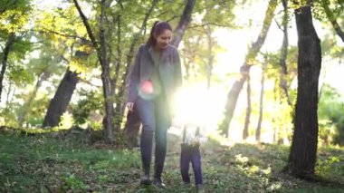 Anne ve küçük kızı güneşli ormanda el ele yürüyorlar. Yüksek kalite 4k görüntü