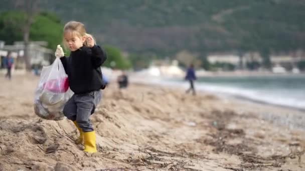 一个小女孩在沙滩上愉快地捡垃圾 在美丽的海滨风景中享受着悠闲的活动 — 图库视频影像