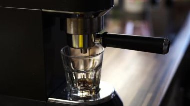 Bir kahve makinesinin yakın çekimi mükemmel bir kahve fincanı oluşturuyor. Sıvı metal kenardan bir bardağa dökülüyor, bu mutfak aletinin karmaşık işleyişini gösteriyor.