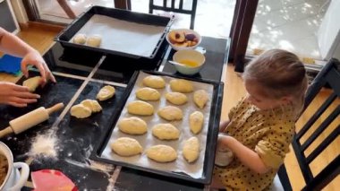 Genç bir kız mutfakta bir masada oturuyor, kurabiye yapmak için mutfak gereçleri ve yemek takımlarını kullanıyor. Bir tarifi takip ediyor, malzemeleri birleştiriyor ve lezzetli bir yemek yapmak için su kullanıyor.