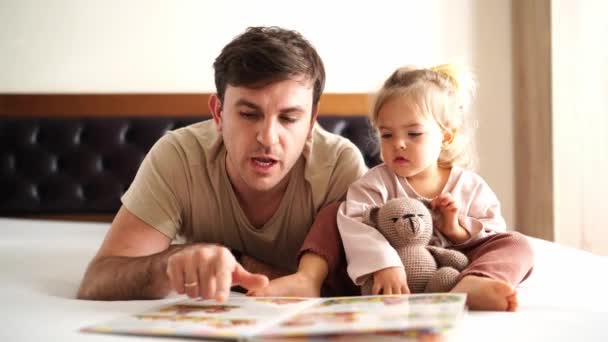 Тато Маленька Донька Читають Книгу Малюнками Лежать Ліжку Проходять Пальцями — стокове відео
