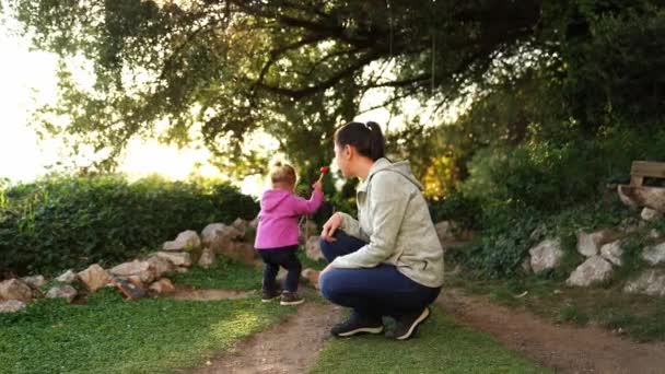 Γελαστή Μητέρα Κάθεται Στο Πάρκο Δίπλα Ένα Κοριτσάκι Που Παίζει — Αρχείο Βίντεο