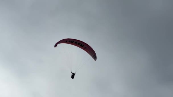 一个人带着生机勃勃的红色降落伞 在空中滑行 一边欣赏着风车 一边欣赏着天空中令人叹为观止的云彩 — 图库视频影像