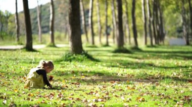 Mutlu küçük bir kız, ağaçlar ve bitkilerle çevrili yeşil çimlerin üzerinde oturmuş, huzurlu atmosferin tadını çıkarıyor.