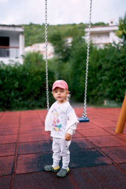 Eşofmanlı küçük bir kız oyun parkında zincirli salıncağın yanında duruyor. Yüksek kalite fotoğraf