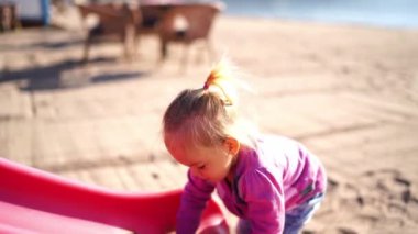 Küçük kız kumsaldaki bir kaydırağa kum döker ve onu siler. Yüksek kalite 4k görüntü
