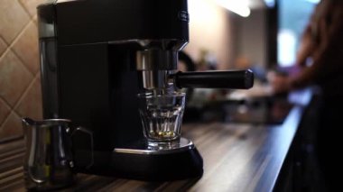 Kahve makinesinden bardağa damlayan kahve damlaları kahve çekirdeklerini öğüten bir adamın arka planında duruyor. Yüksek kalite 4k görüntü