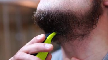 Bir adam tıraş makinesiyle sakalını tıraş ediyor. Yüksek kalite