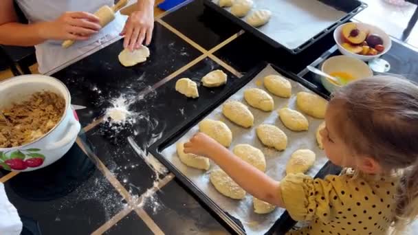若い女の子は食材や調理器具を使ってパンを作るテーブルに座っている 彼女はおいしい料理を作るためにレシピをフォローしています — ストック動画
