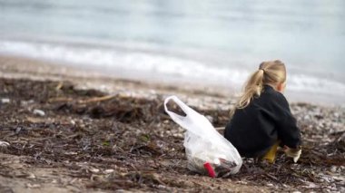 Plajda elinde plastik bir torbayla oturan genç bir kız dalgaları seyrediyor ve saçlarında rüzgarı hissediyor. O mutlu ve doğanın güzelliğiyle çevrili.