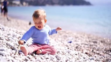 Küçük çocuk sahilde otururken bir sopayla çakıl taşlarına çarpıyor. Yüksek kalite 4k görüntü