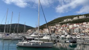 Suda yüzen sayısız tekneleri olan bir marina. Arka planda bulutlu bir gökyüzünün altında görkemli bir dağ var.