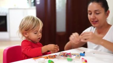 Anne ve küçük kızı masada çok renkli plastiklerin heykelciklerini yontuyorlar. Yüksek kalite 4k görüntü