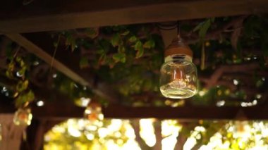 Şeffaf bir lambadaki ampul güneşteki bir pergola 'nın tavanında asılı. Yüksek kalite 4k görüntü