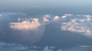 Gün batımında bir uçak penceresinden atmosferik manzaradaki kümülüs bulutlarını gözlemlemek ufkun ve meteorolojik fenomenin çarpıcı bir görüntüsünü sergiliyor.