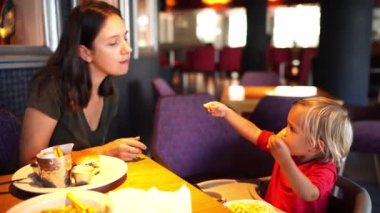 Küçük kız bir restoranda masada otururken annesine patates kızartması ikram ediyor. Yüksek kalite 4k görüntü