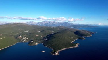 Okyanusun ortasındaki dağlarla çevrili küçük bir adanın havadan görünüşü, gökyüzünü yansıtan su ve bulutlar nefes kesici bir doğal manzara yaratıyor.