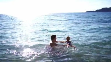 Babam küçük bir kızı karnından tutup denizde yüzdürüyor. Yüksek kalite 4k görüntü