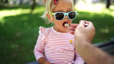 Babam parkta bir bankta kaşıkla küçük bir kızı yulaf lapasıyla besler. Yüksek kalite 4k görüntü