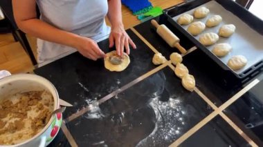 Bir kadın yemek malzemeleri ve yemek tarifi için su kullanarak masada hamur hazırlıyor. O, yemek takımları, yemek takımları ve fırında fırın kullanarak mutfağında bir tabak pişiriyor.