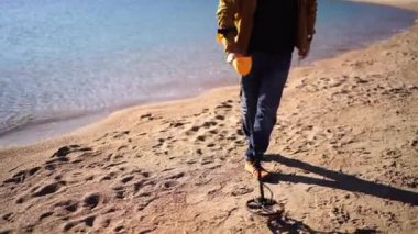 Adam deniz kenarındaki kumlu bir sahili metal dedektörüyle süpürüyor. Yüksek kalite 4k görüntü