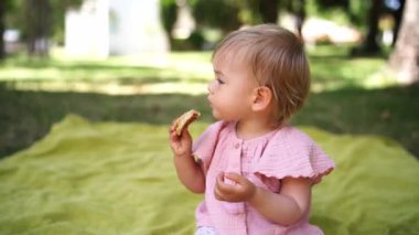 Küçük kız bahçedeki bir yatak örtüsünde oturmuş krep yiyor. Yüksek kalite 4k görüntü