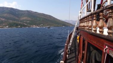 Deniz mimarisi tarafından tasarlanmış bir su aracı, arka planda görkemli dağlar olan sakin bir gölde, bulutlu, berrak bir gökyüzünün altında yüzüyor.