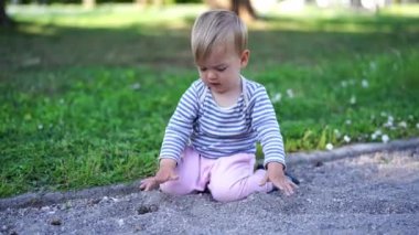 Küçük bebek parkta bir patikada dizlerinin üzerinde oturur ve elleriyle kürek çeker. Yüksek kalite 4k görüntü