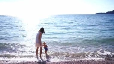 Anne ve küçük bir kız sığ sularda deniz dalgalarında yürüyorlar. Yüksek kalite 4k görüntü