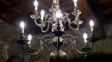 Tavandan sarkan mumlarla süslenmiş bir avize. Zarif ışıklandırma, karmaşık metal ve bileşik malzeme yapısı sergileniyor.
