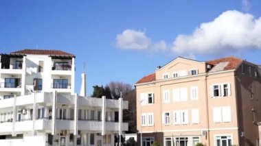 Göz kamaştırıcı, kırmızı çatılı beyaz bir bina daha küçük bir yapının yanında duruyor, mavi gökyüzüne karşı tüylü beyaz bulutlarla benekli bir manzara yaratıyor.
