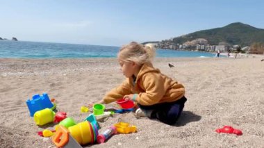 Bir çocuk kumsalda kumsalda oynarken eğleniyor, açık gökyüzünün altında su parlıyor. Manzara huzurlu, dinlenmek için sakin ve mutlu bir atmosfer yaratıyor.