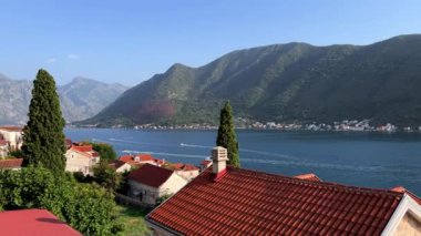 Doğal bir manzaraya yuva yapmış, arka planda görkemli dağlar olan sakin bir göle bakan, kırmızı kiremitli bir çatı olan bir rıhtım evi.