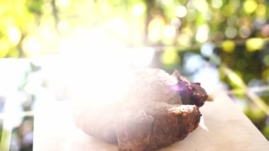 Biftek, parlak güneş ışığında bir balkondaki bir masanın tahta kesme tahtasının üzerinde yatıyor. Yüksek kaliteli FullHD görüntüler