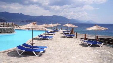 Rüzgar, havuz kenarındaki güneş pansiyonlarının yanındaki saman şemsiyelerini sallıyor. Yüksek kalite 4k görüntü