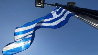 Elektrikli mavi ve beyaz bir bayrak rüzgarda dalgalanıyor bir olayı sembolize ediyor. Bayrak gökyüzü, sokak lambaları ve makine aydınlatma armatürlerine karşıdır.