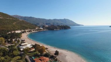Arka planda dağlar, geniş bir su kütlesi, kıyı boyunca uzanan ağaçlar ve manzaralı doğal manzara.