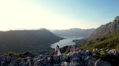Bir çift dağın tepesinden nefes kesici bir göl manzarasının tadını çıkarıyor. Gökyüzü birkaç kabarık bulutla berrak, çarpıcı bir doğal manzara yaratıyor.