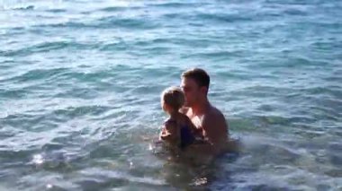Babam küçük bir kızı kaldırır ve denize indirir. Onu koltukaltlarından tutarak. Yüksek kalite 4k görüntü