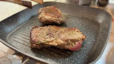 Birisi tavada bir parça domuz eti pişiriyor, lezzetli bir yemek hazırlıyor. Cızırdayan ses mutfağı kırmızı et kokusuyla dolduruyor.