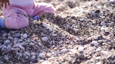 Küçük bebek çakıl taşlarını kazıyor, topluyor ve fırlatıyor, dizlerinin üzerinde oturuyor. Yüksek kalite 4k görüntü