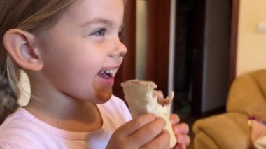 Yanağında, burnunda ve ağzında çikolata lekesi olan küçük bir kız büyük bir gülümseme ve dağınık saçlarıyla aptal bir surat yapıyor.