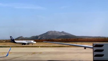 Arka planda görkemli bir dağ bulunan bir araç asfalt pistinden gökyüzüne doğru yükseliyor. Arazi ağaçlar, bulutlar ve uzak bir ufuk içerir.