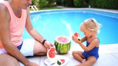 Küçük kız parçalarını dağıtan babasının yanında bir parça karpuz yiyor. Yüksek kalite 4k görüntü