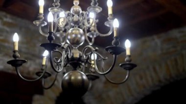 Tavandan sarkan mumlarla birlikte metal bir avize, karanlık odadaki moda aksesuarıdır, simetri yaratır ve olaya renk ve gölge katar.