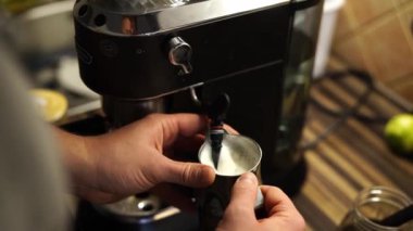 Bir kişi kahve fincanına bir mutfak aleti kullanarak süt ekliyor. Sıvı, içecekle karışır ve başparmağının dokunuşuyla lezzetli bir tarif yaratır.
