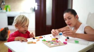 Gülümseyen anne, küçük bir kızın önüne plastik bir köpek koyar. Yüksek kalite 4k görüntü